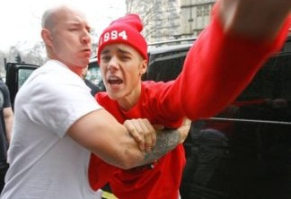 Justin Bieber|Bieber estava deixando o hotel Langham quando os paparazzis o cercaram. Ele se irritou e tentou partir pra cima de um, mas foi impedido pelo segurança, como vemos na foto.